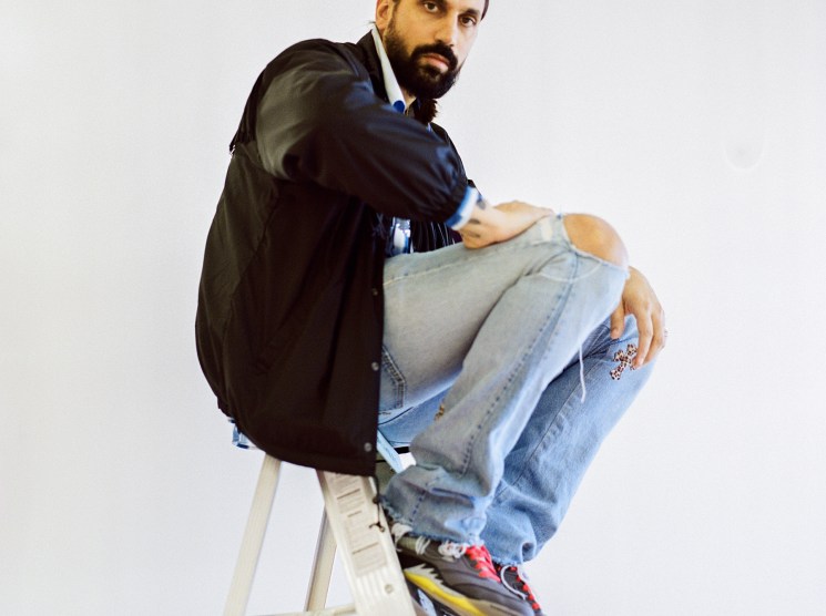 Ben Gorham, founder of Byredo, sits on a ladder wearing a black jacket and distressed jeans.