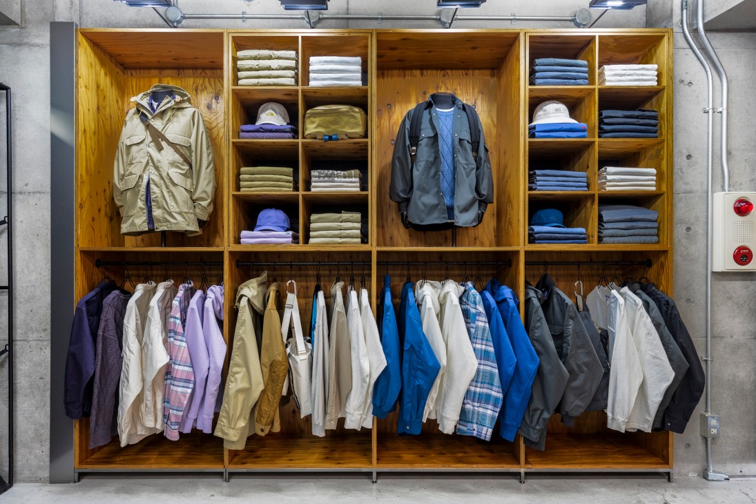 Organized display of outdoor clothing in wooden retail shelving with jackets hanging and folded items on shelves