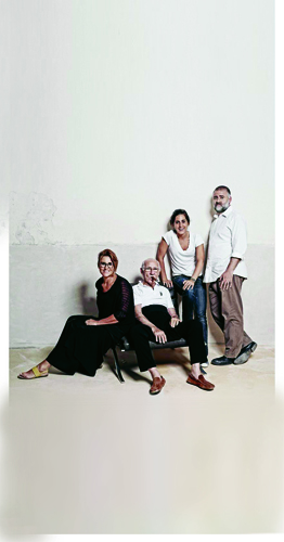 Group of four people posing against a white wall in casual business attire.