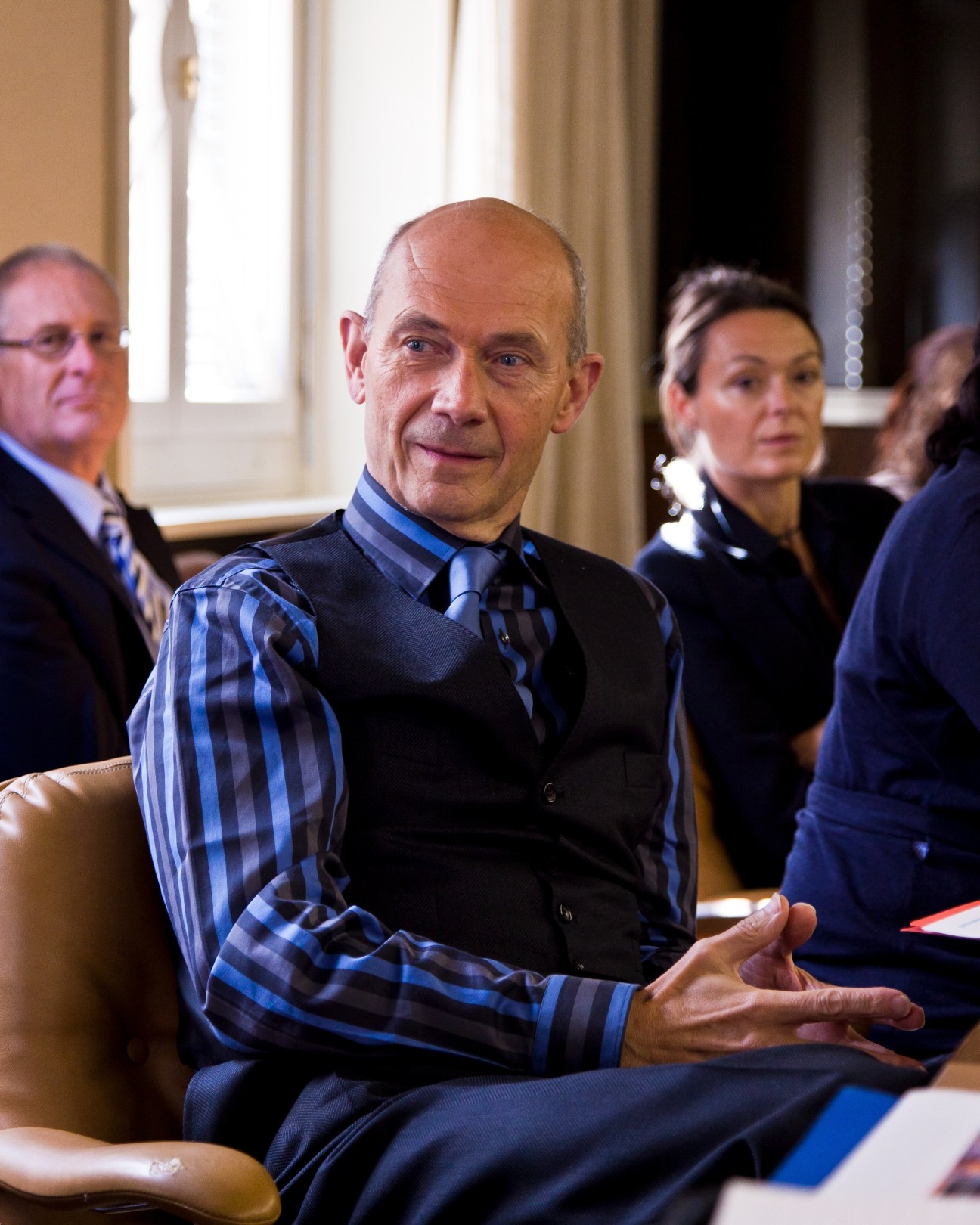 Pascal Lamy seated in a formal meeting room with other officials in the background.