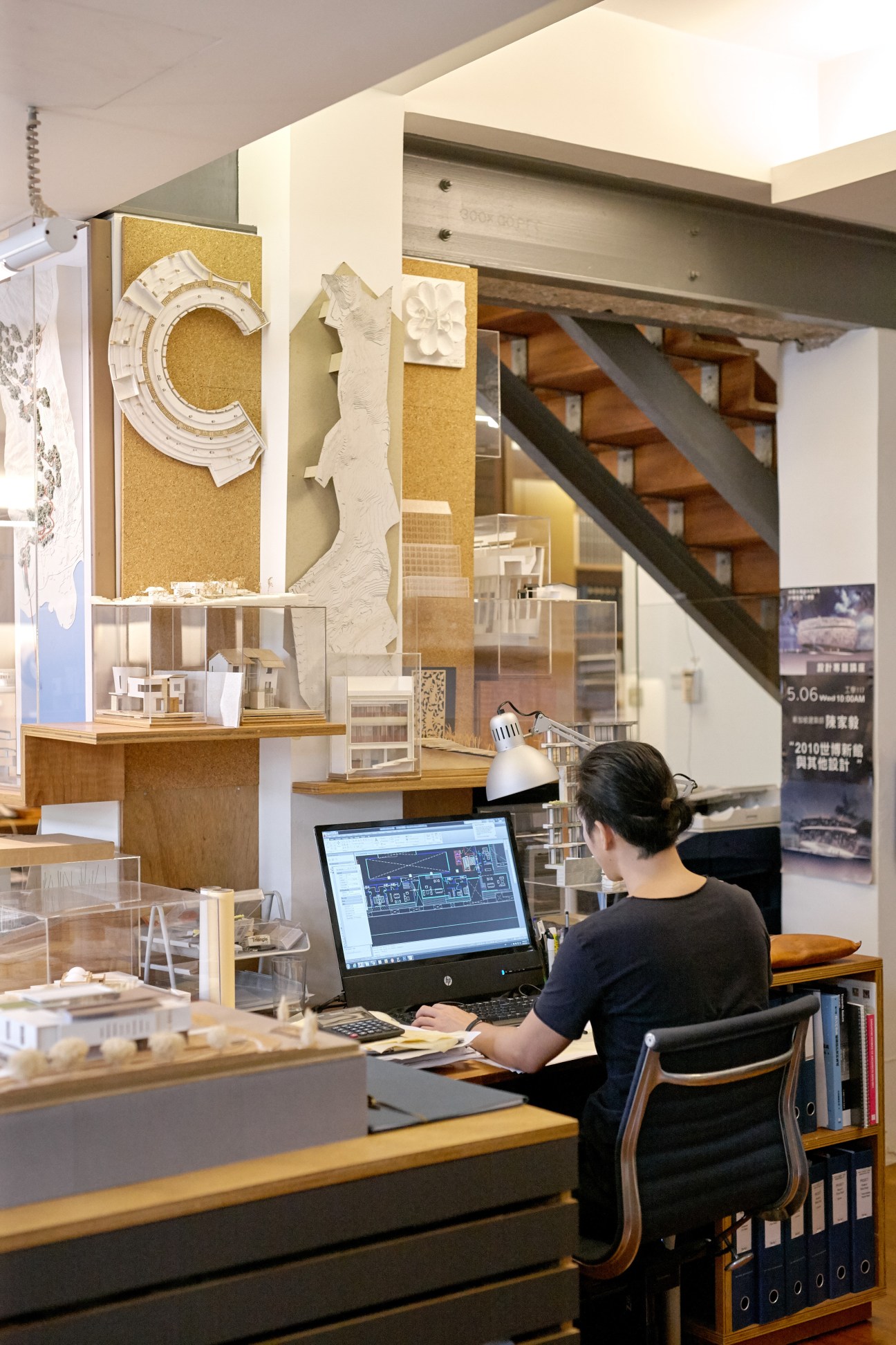 Designer working at desk with laptop surrounded by architectural models and material samples in studio.