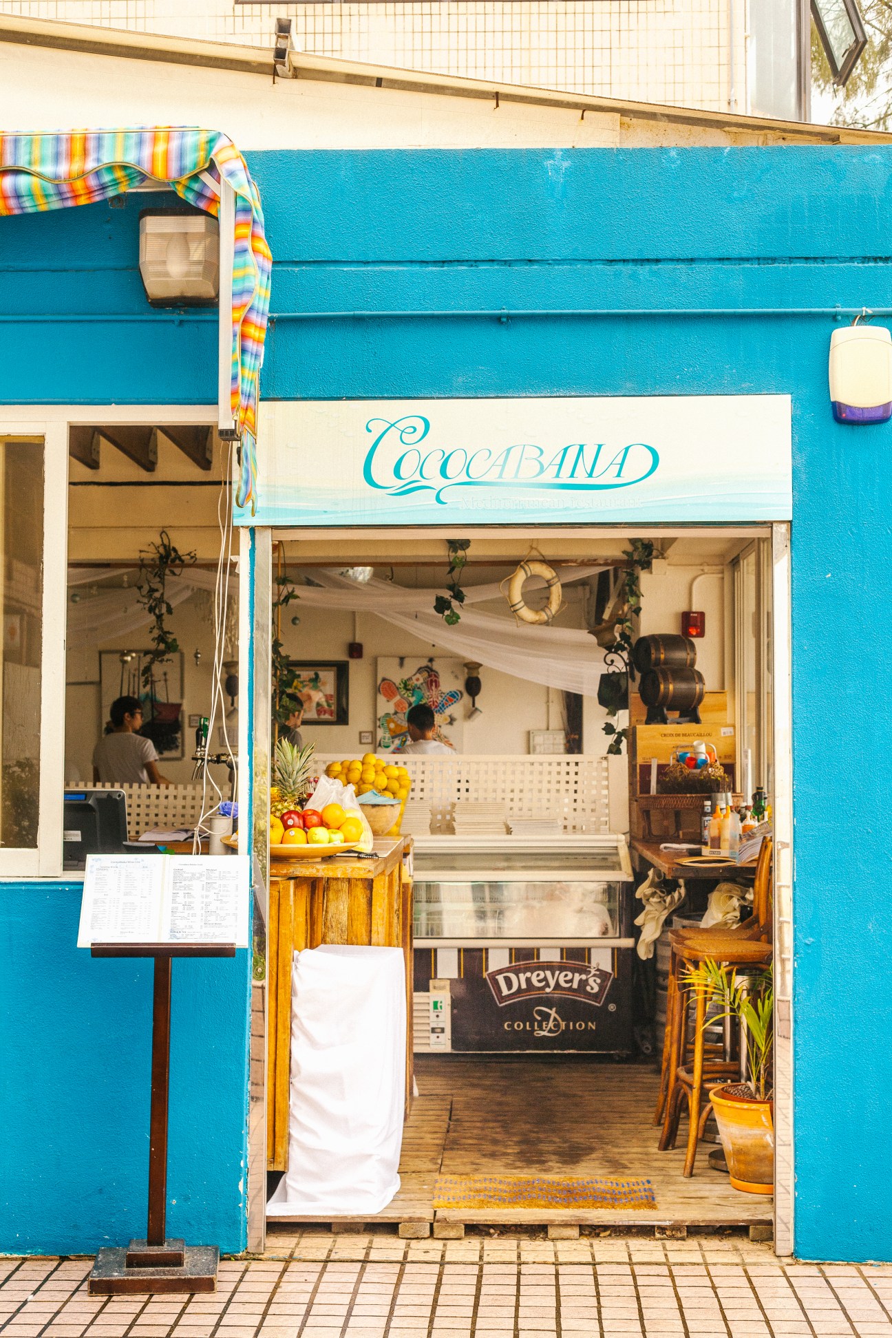 Bright turquoise storefront of Coccoband ice cream shop in Shek O with colorful striped awning and fresh fruit display.