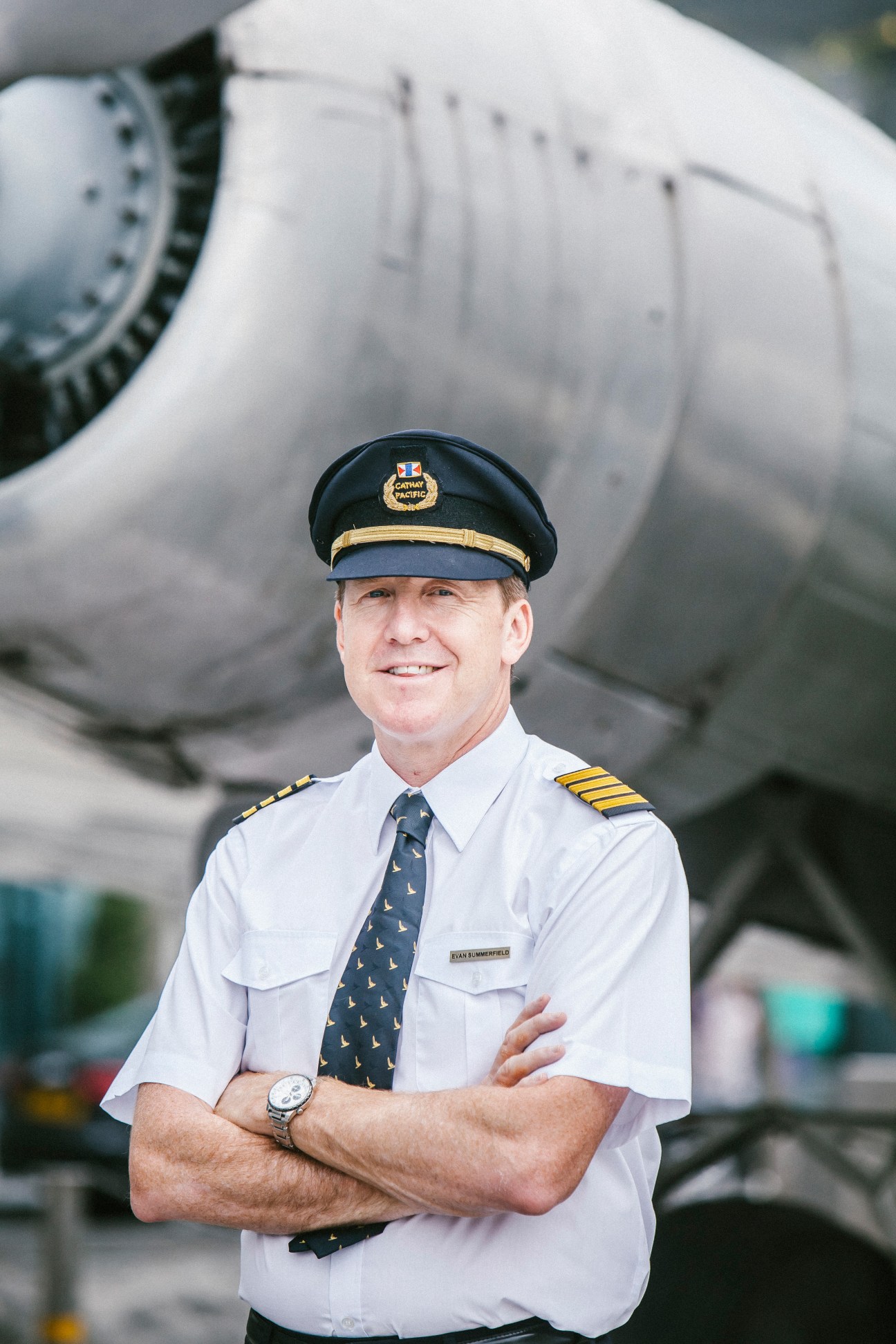 Cathay Pacific captain Evan Summerfield in uniform standing before aircraft engine.