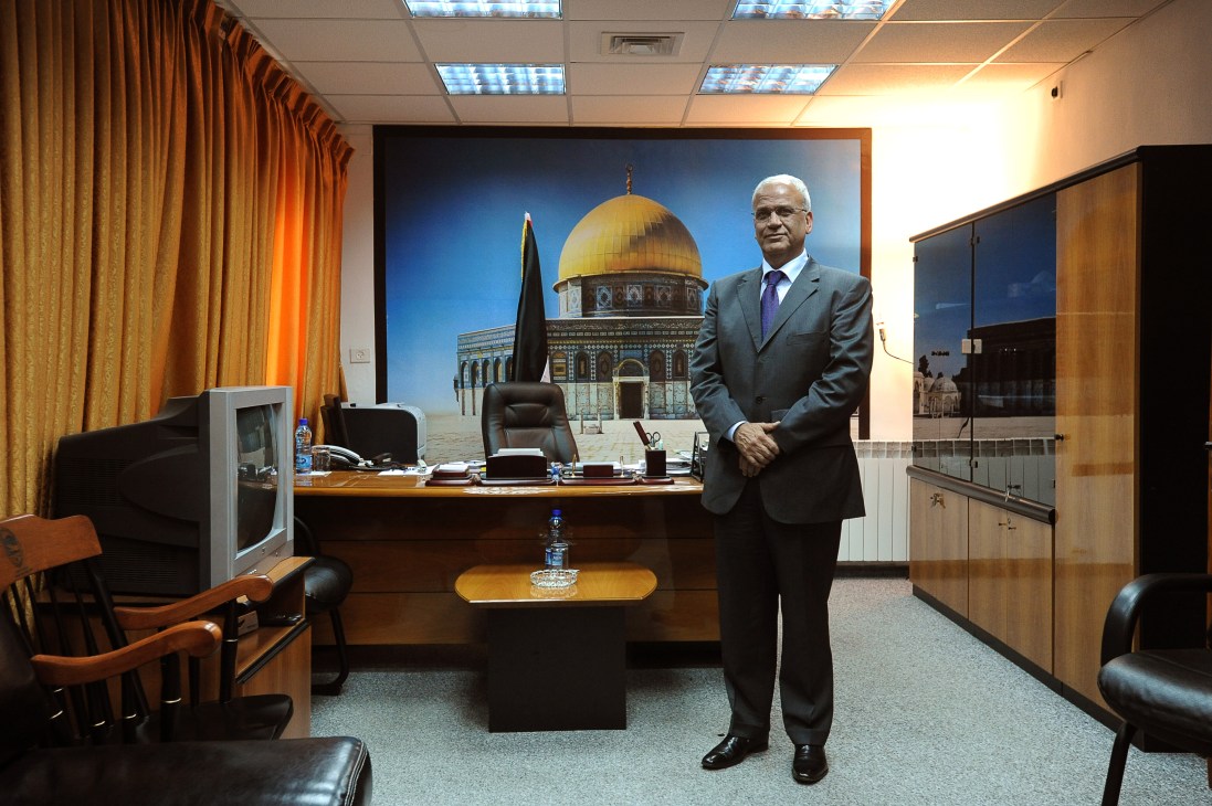 Palestinian negotiator Saeb Erakat standing in his office in Ramallah with the Dome of the Rock displayed on the wall behind his desk.