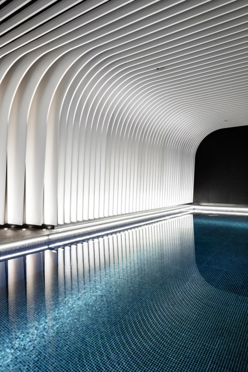 Interior view of an arched swimming pool with ribbed white ceiling and blue mosaic tile flooring.