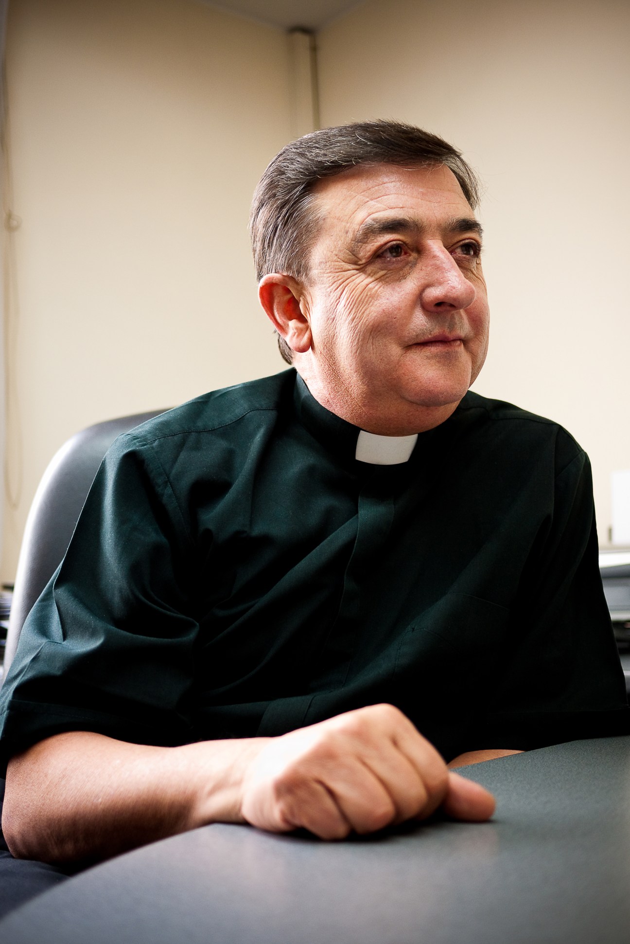 Colombian priest Dario Echeverri in black clerical attire seated at a table.