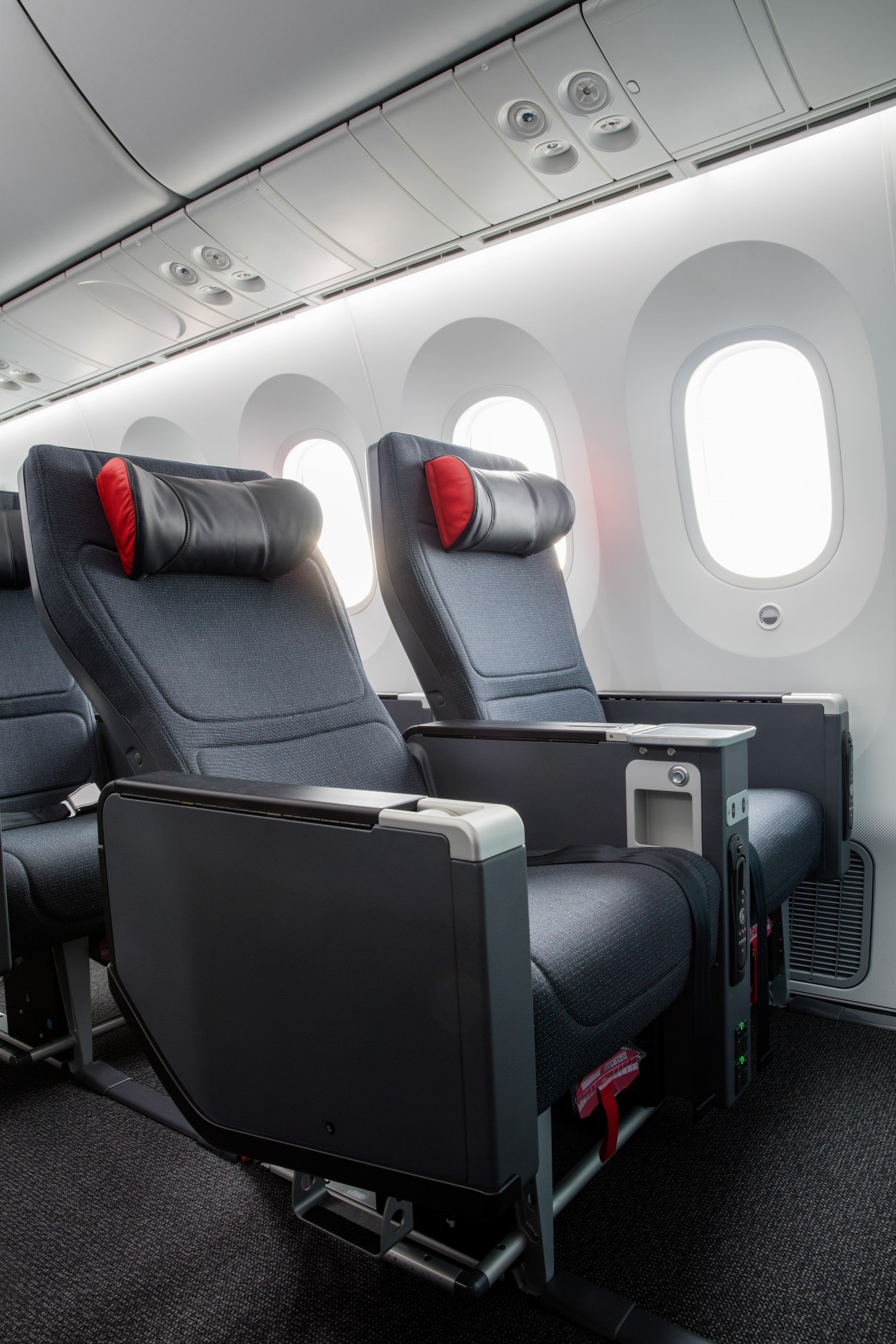 Air Canada Premium Economy cabin with reclining seats, red pillows, and illuminated oval windows.