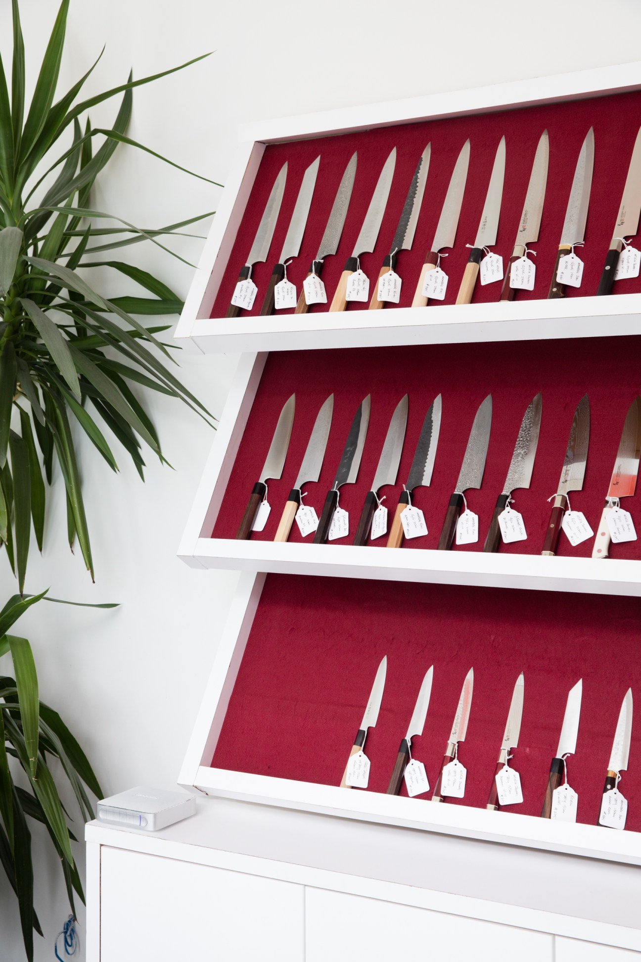 Display of handmade Japanese kitchen knives with various blade styles arranged on red velvet shelves at Knife Toronto.