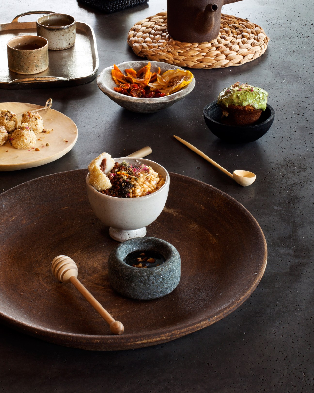 Styled food spread with ceramic dishes, dried citrus, grains, and fresh herbs on dark surface.