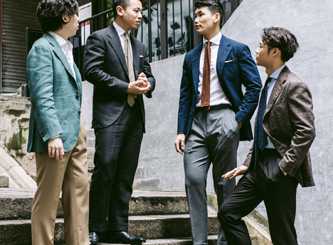 Chris Tang and colleagues at Prologue menswear shop in Hong Kong discussing made-to-order suits on exterior steps.