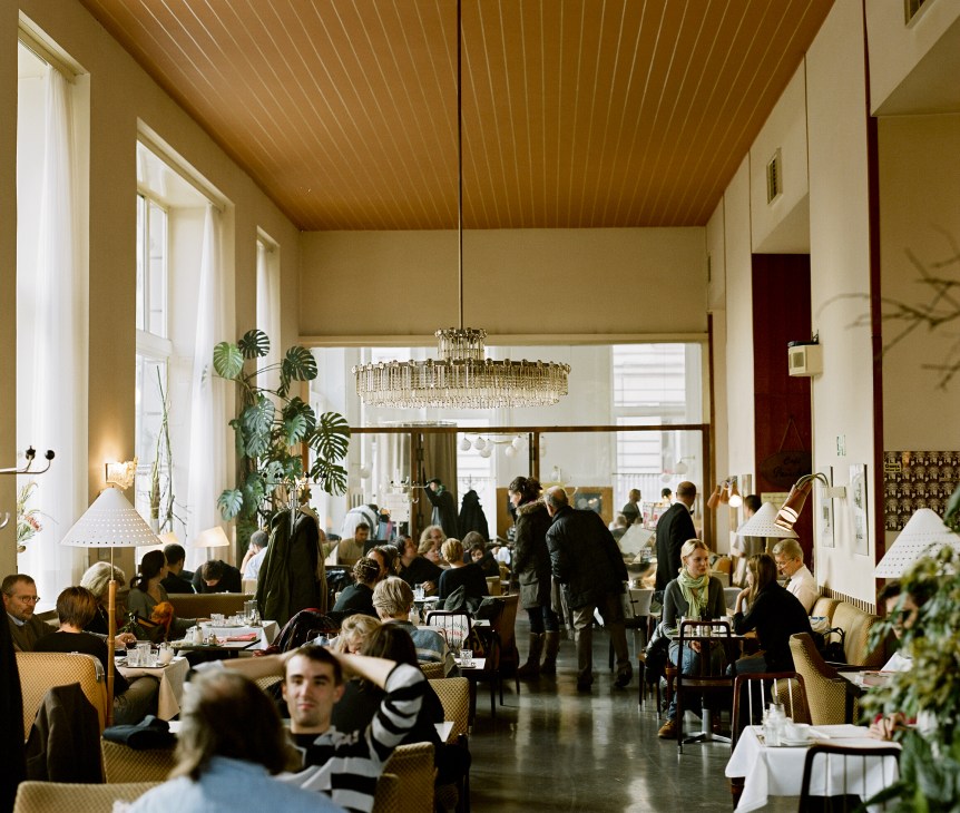 Interior of a Viennese café with high ceilings, crystal chandelier, warm lighting, and diners seated at tables.