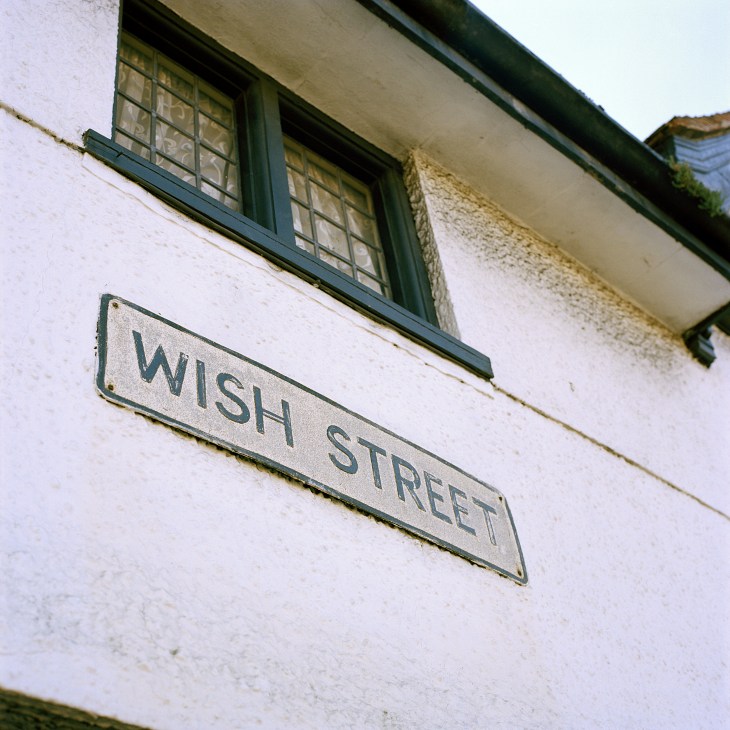 Wish Street sign on a white-washed historic building with green-framed windows in Rye, England.