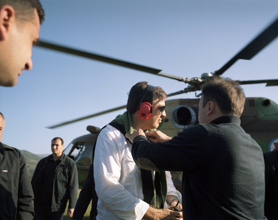 Mikheil Saakashvili wearing sunglasses and headphones stands near a helicopter with advisers.