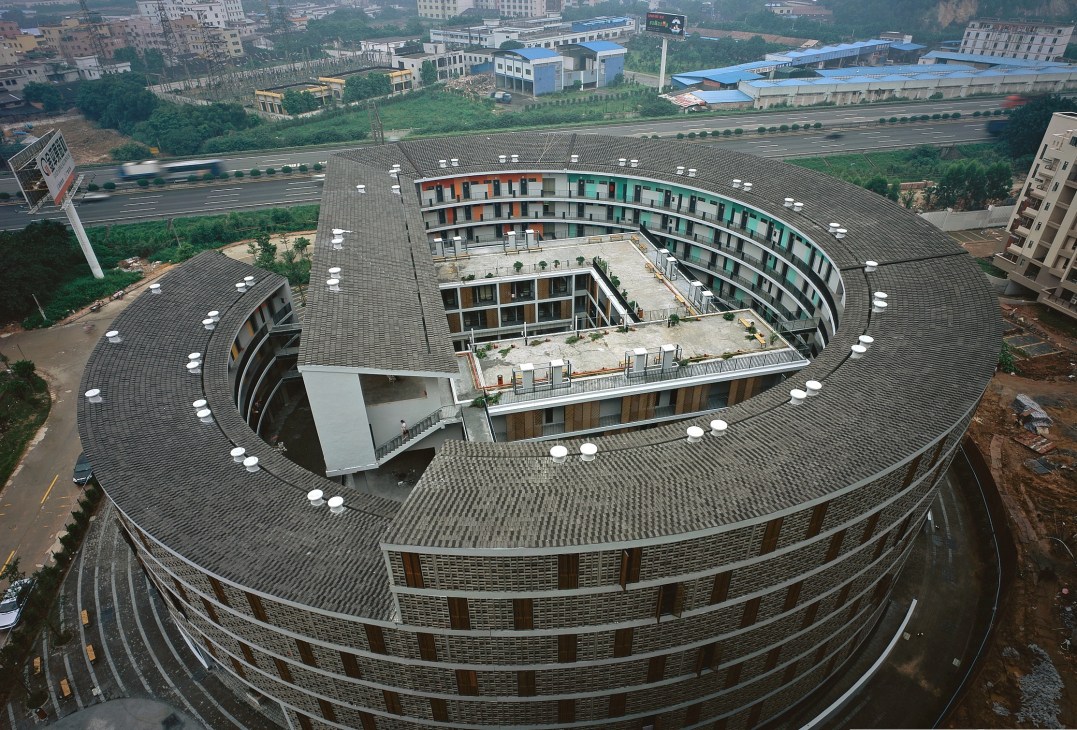 Aerial view of a circular residential building with curved architecture and central courtyard in an urban setting.