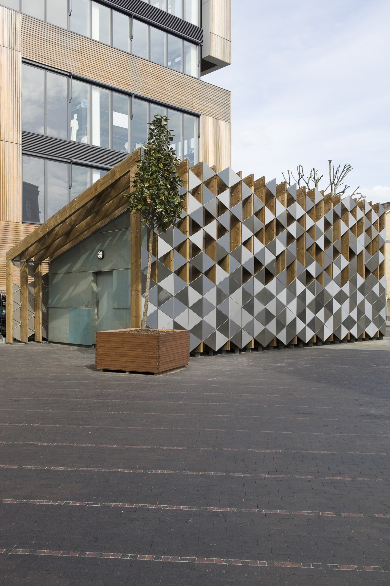 Modern residential tower with corrugated metal cladding and geometric lattice screen at street level in Manchester.