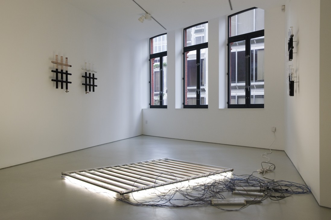Minimalist interior space with large windows, wall-mounted geometric art, and illuminated bed frame on concrete floor.