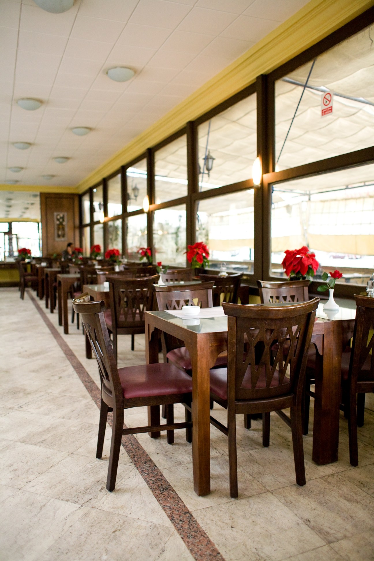 Interior of Petit Palmyra restaurant with wooden chairs, red flowers, and large windows overlooking the street.
