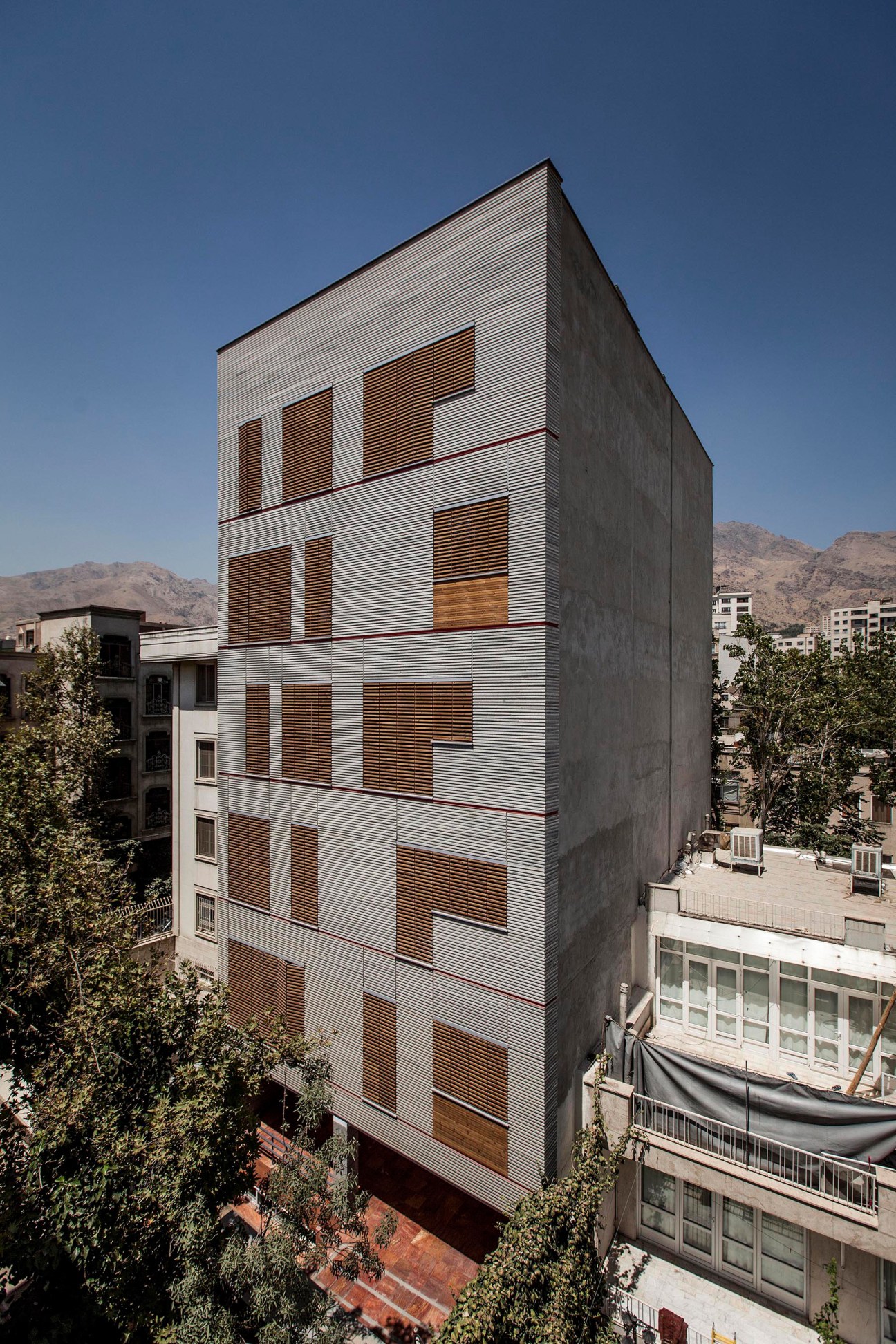 Modern residential building with white and dark corrugated metal facade and wooden louvered windows in Tehran.