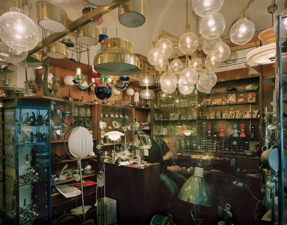 Interior of a vintage design shop with brass and glass pendant lights, wooden shelving displaying ceramics and decorative objects.