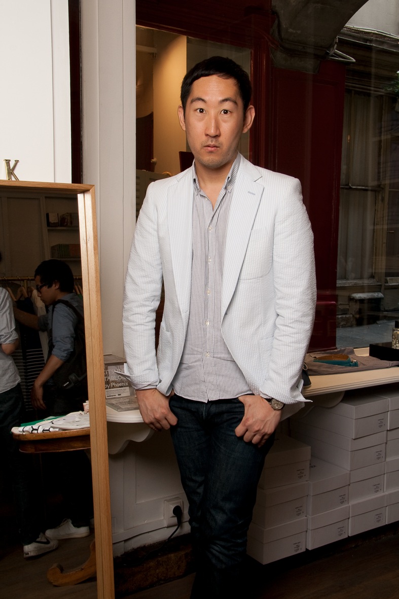 Man in light grey blazer and striped shirt standing in modern retail interior with wooden fixtures.
