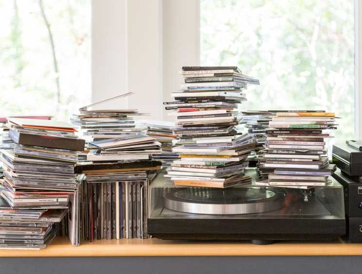 Stacks of CDs and music albums arranged on a wooden shelf next to a turntable and speaker.
