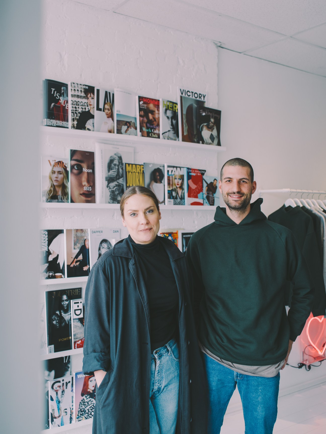 Two people standing in front of a wall displaying magazine covers and posters in Soop Soop retail shop.