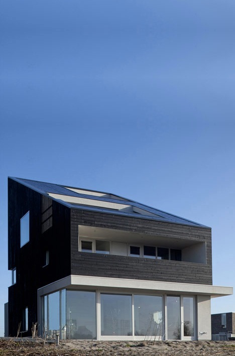 Modern three-storey residential home on Amsterdam island with dark wood cladding, solar panels, and large glazed ground floor.