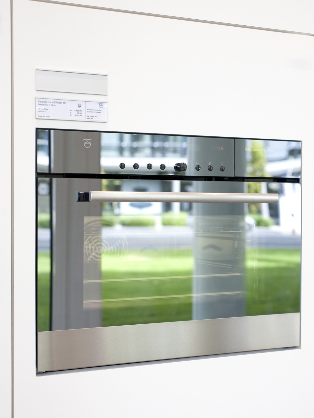 V-Zug combi steamer oven with stainless steel finish and control panel mounted in white wall.