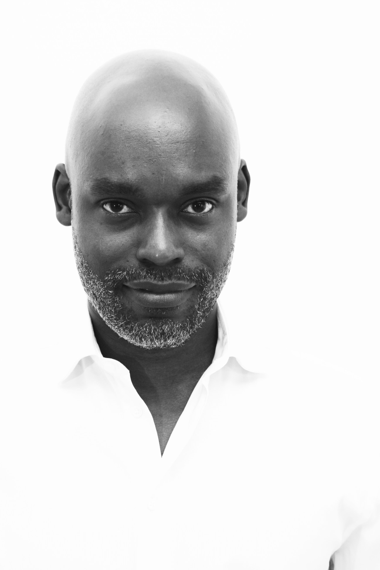 Black and white portrait photograph of a bald man with a grey beard wearing a white shirt.