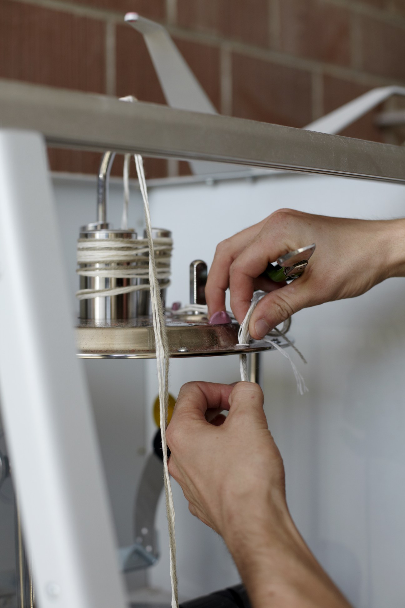 Hands mounting linen base onto wooden frame with metal clamp at Kramis carpet workshop.