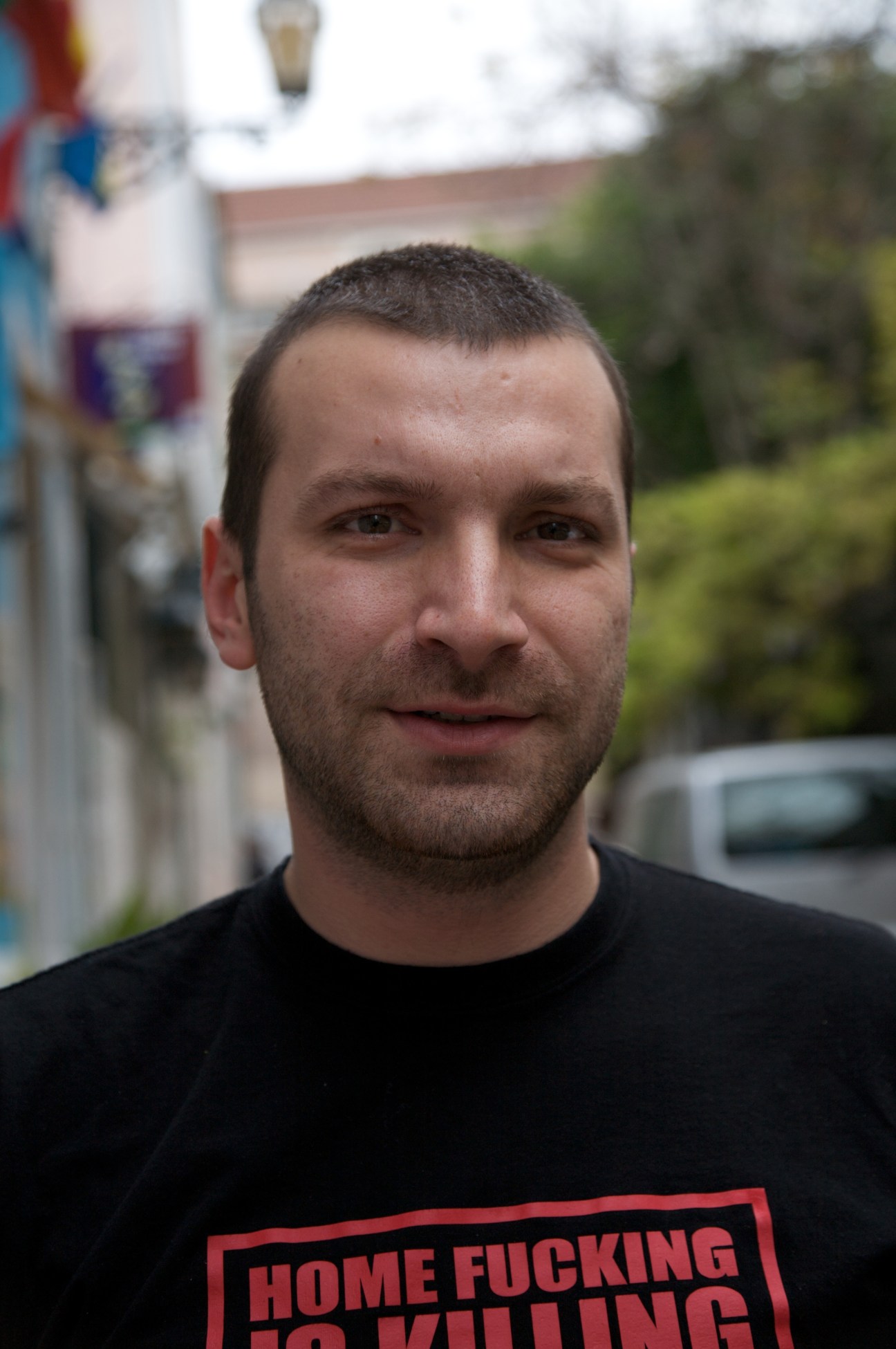 Man wearing black t-shirt with red text standing outside in Lisbon neighbourhood
