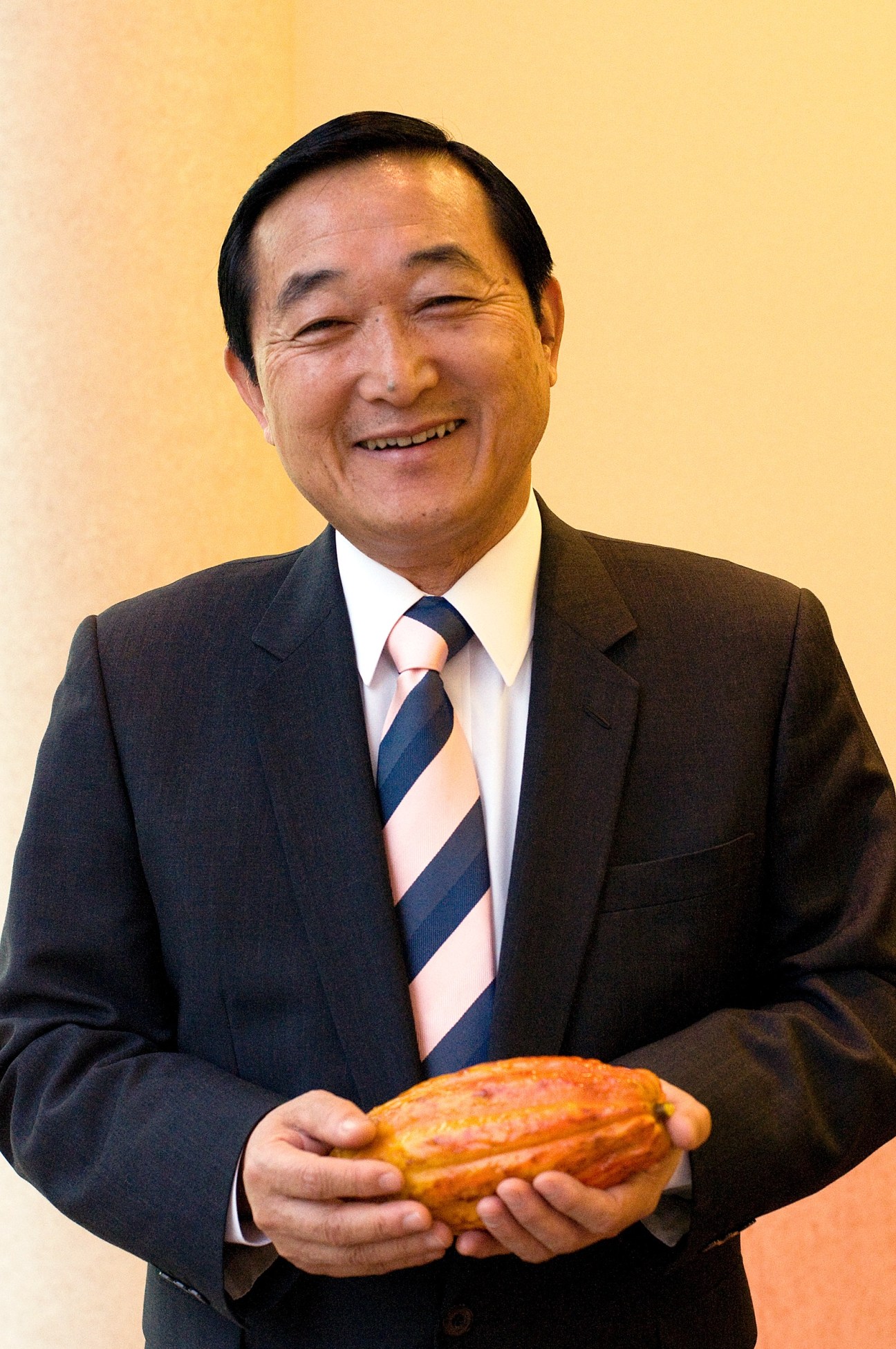 Yasuhiro Yamazaki, founder and president of Royce' Confect, holds a chocolate-coated pastry while smiling.