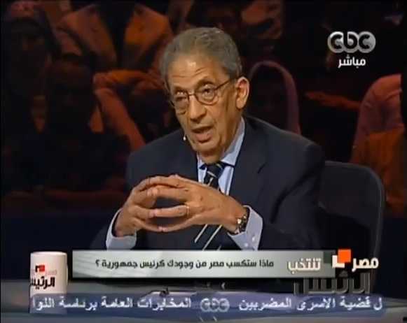 Man in glasses and blue suit speaking on Egyptian CBC television news program.