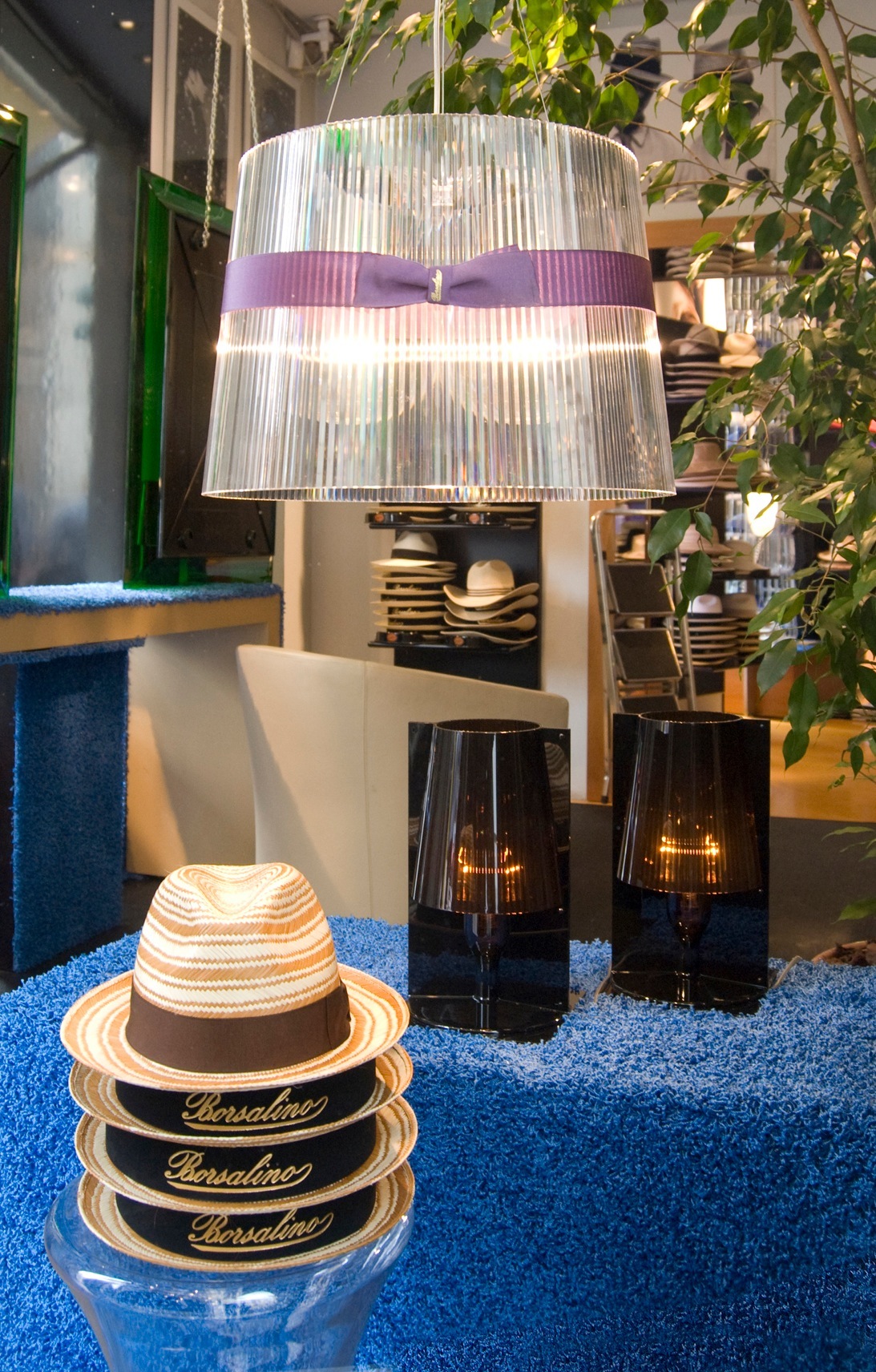 Borsalino straw Panama hats stacked on display with a decorative lamp in a hat shop window.