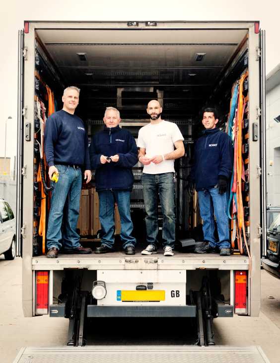 Four Momart staff members stand inside an open delivery truck filled with orange protective padding and wooden crates.