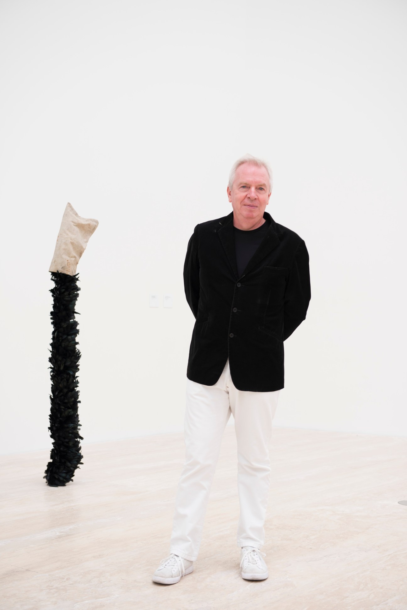 Architect David Chipperfield standing next to a sculptural artwork with black base and cream top element.