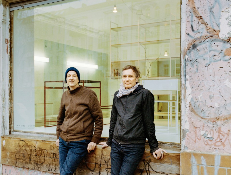 Two men stand outside a storefront with minimalist shelving visible through the window on Berlin's Danziger Strasse.