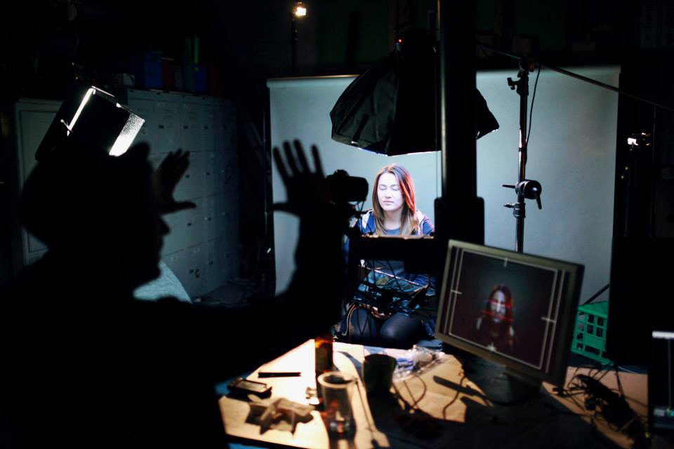 Animation studio workspace with person at desk surrounded by lighting equipment and monitors displaying digital artwork.