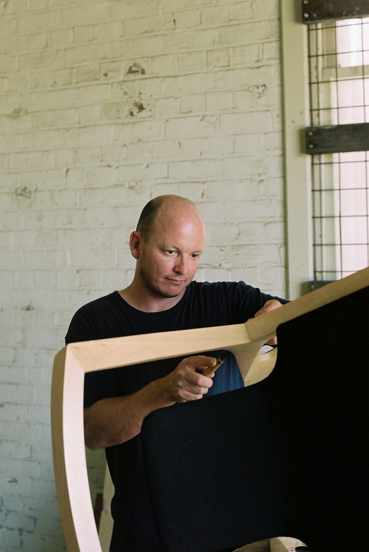 Jon Goulder, a furniture designer, examining a wooden chair frame in his workshop.