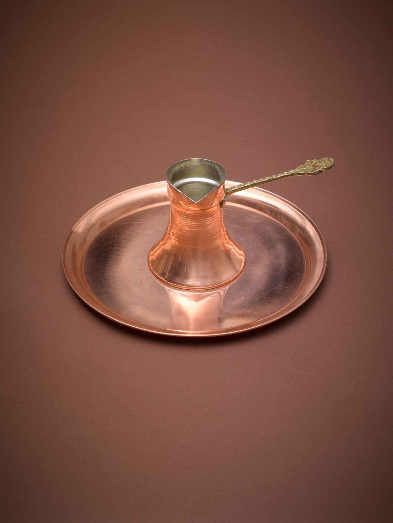 Copper tray and traditional coffee pot with brass handle on brown background.