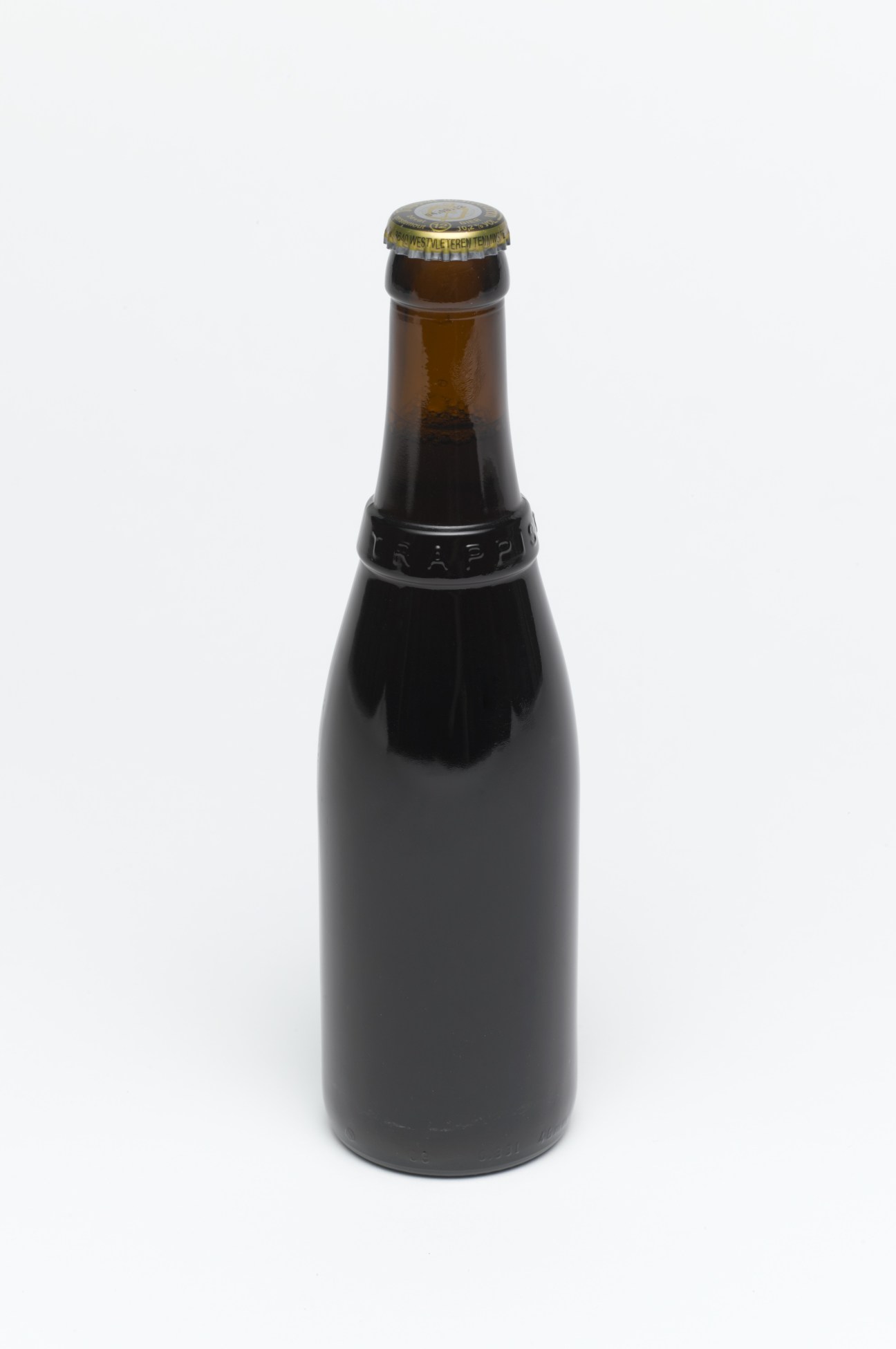 A dark Trappist beer bottle with a gold foil-lined cap against a white background.
