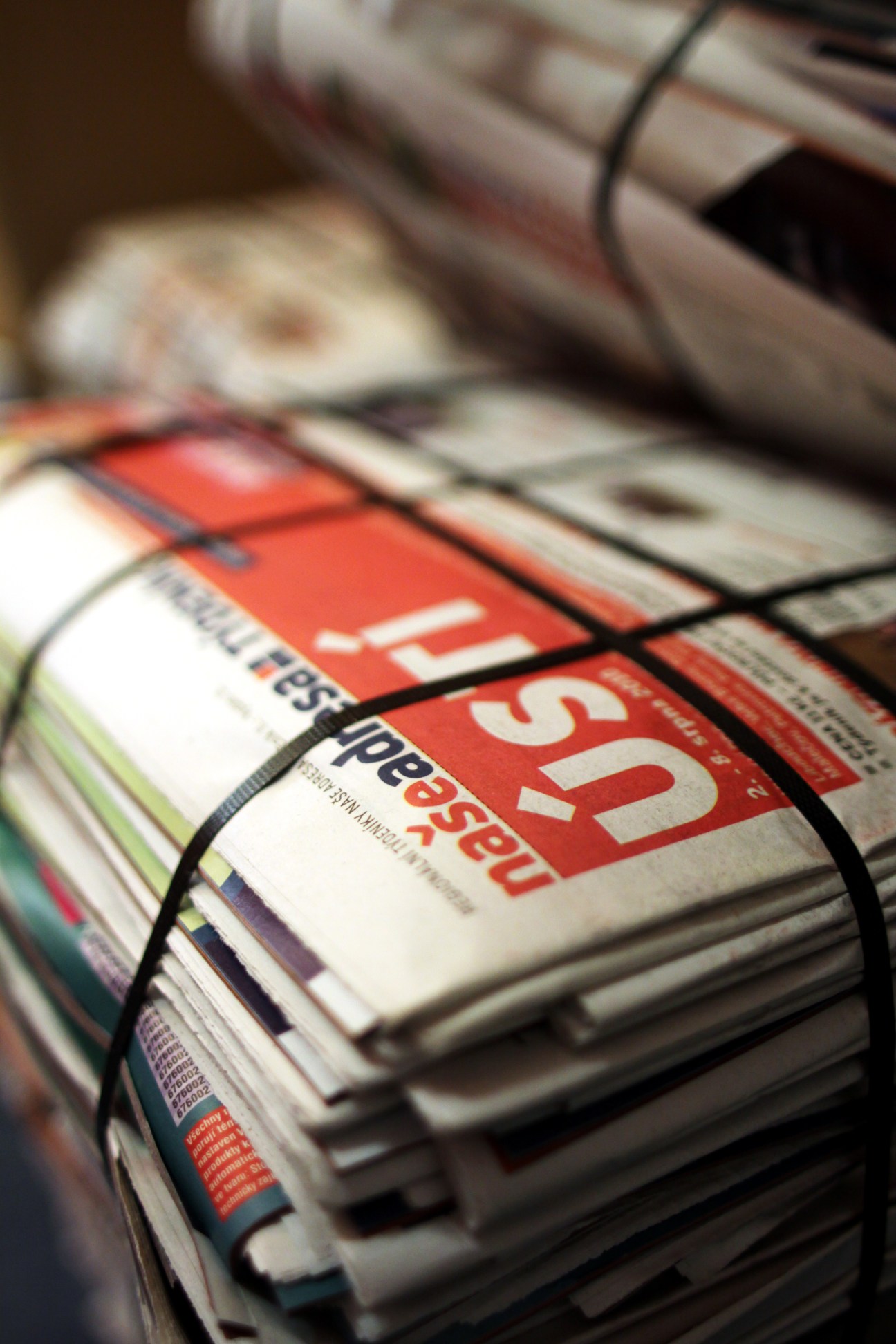 Stack of local newspapers bound together, showing red mastheads and publication covers.