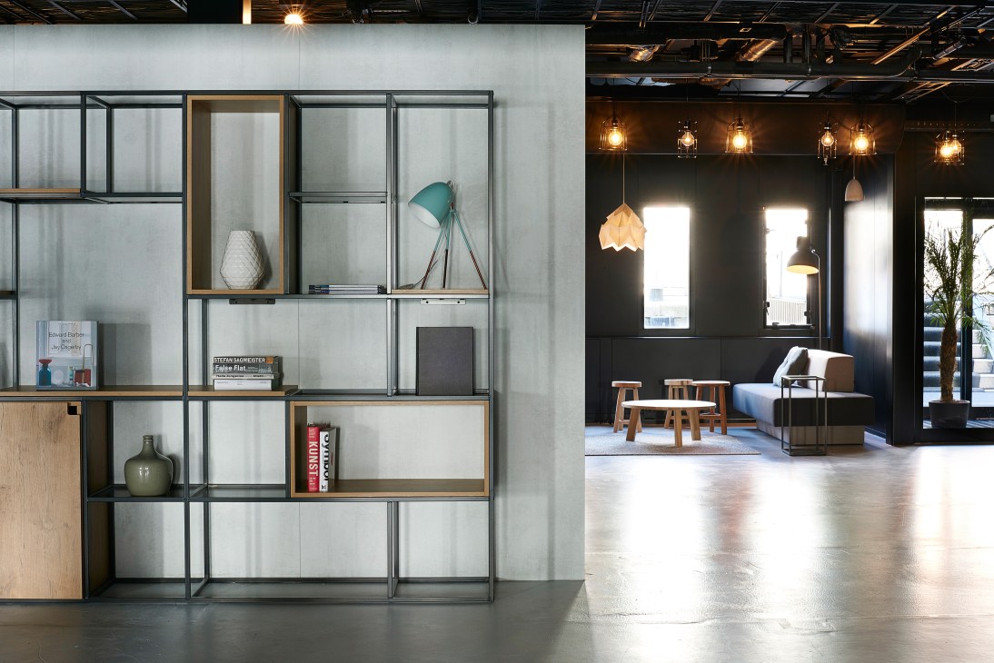 Modern hotel lobby with modular shelving, pendant lights, wooden seating, and dark accent walls.