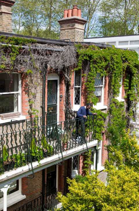 A man in a navy jacket tends to ivy-covered walls of a brick Marylebone townhouse with white-trimmed windows.