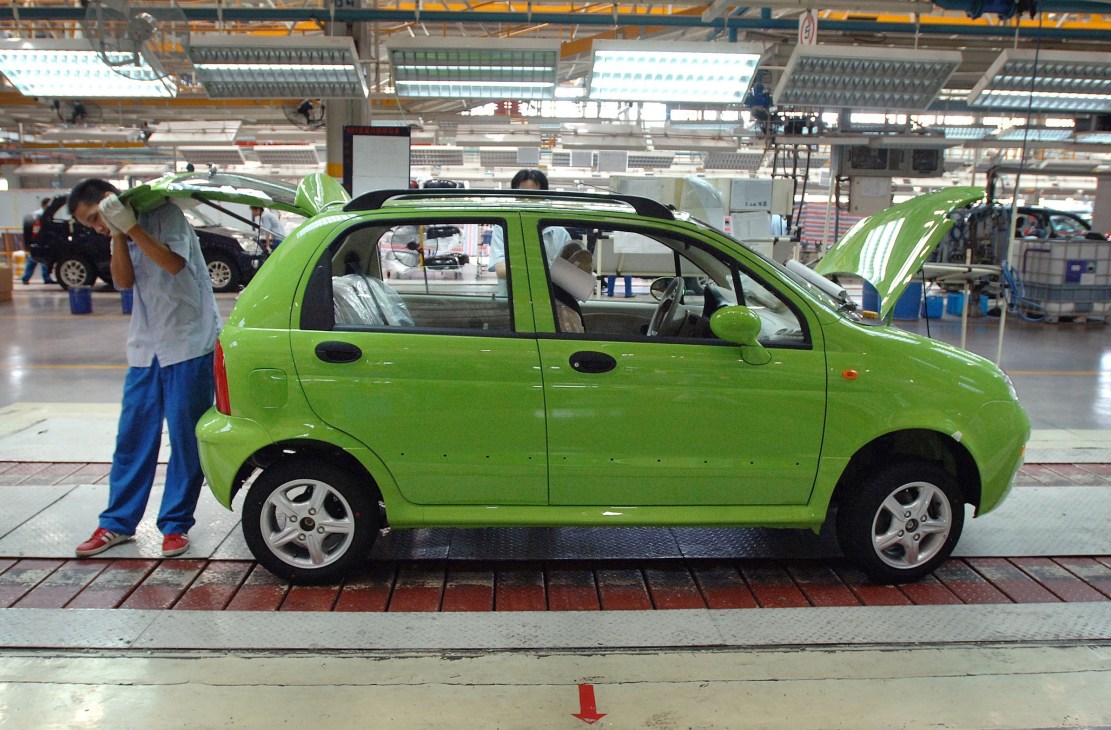 Bright green Chery electric car on factory assembly line with worker inspecting vehicle.