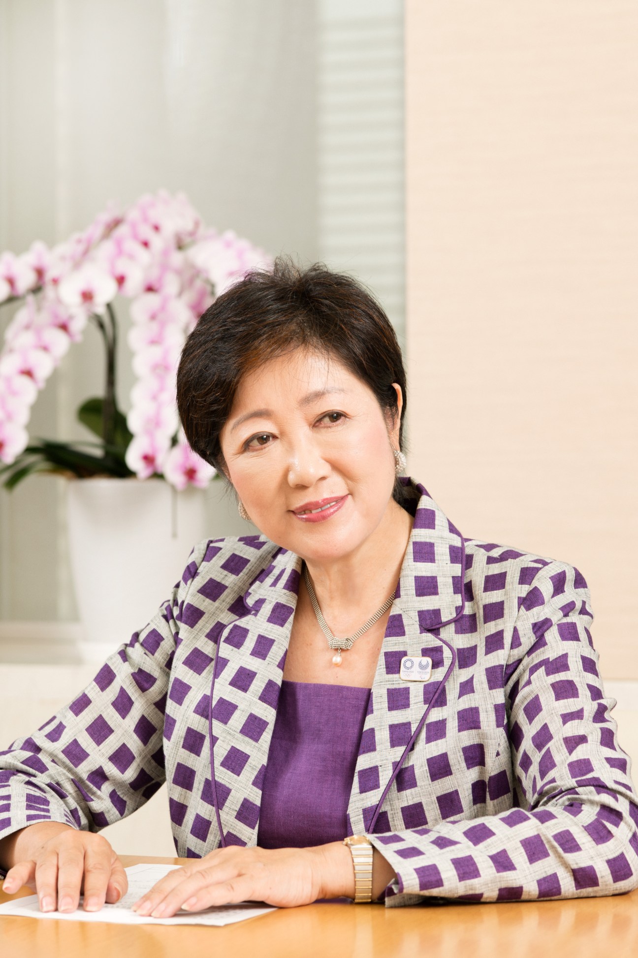 Yuriko Koike, Tokyo's governor, sits at a desk with pink orchids in the background.