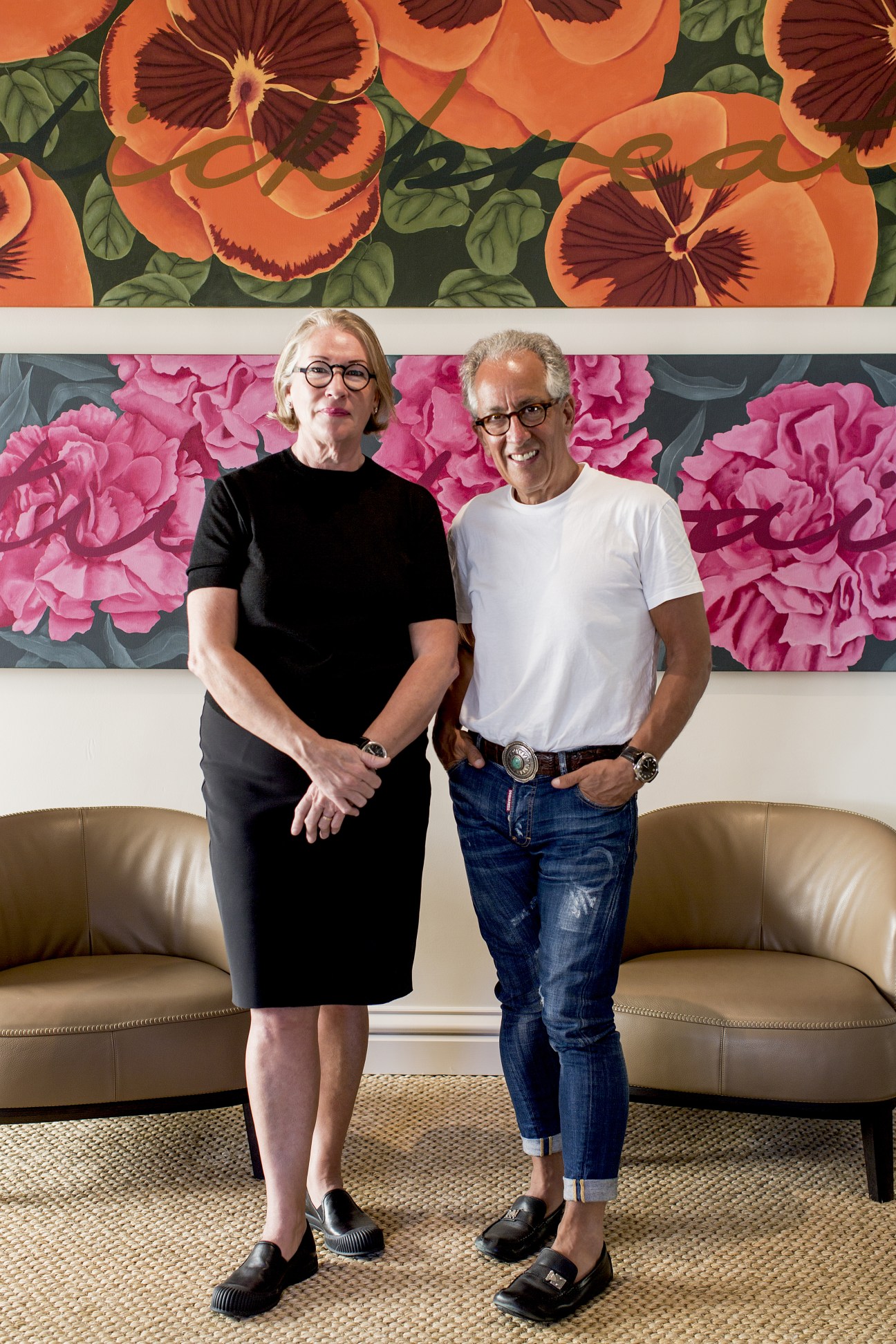 Two people standing in front of colorful floral artwork in an interior setting.