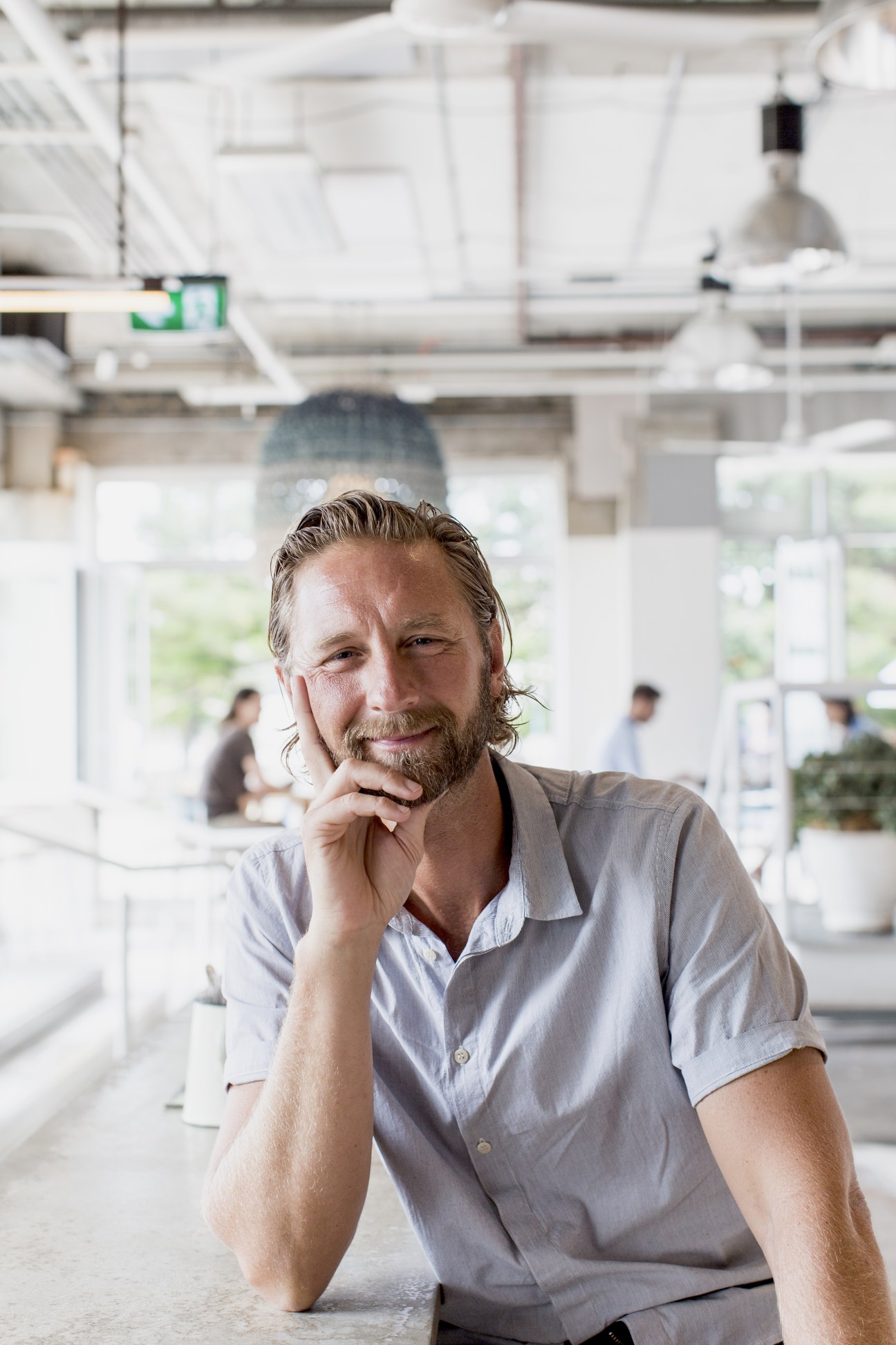 Justin Hemmes, CEO of Merivale Group, poses in a modern restaurant space with hand to face.