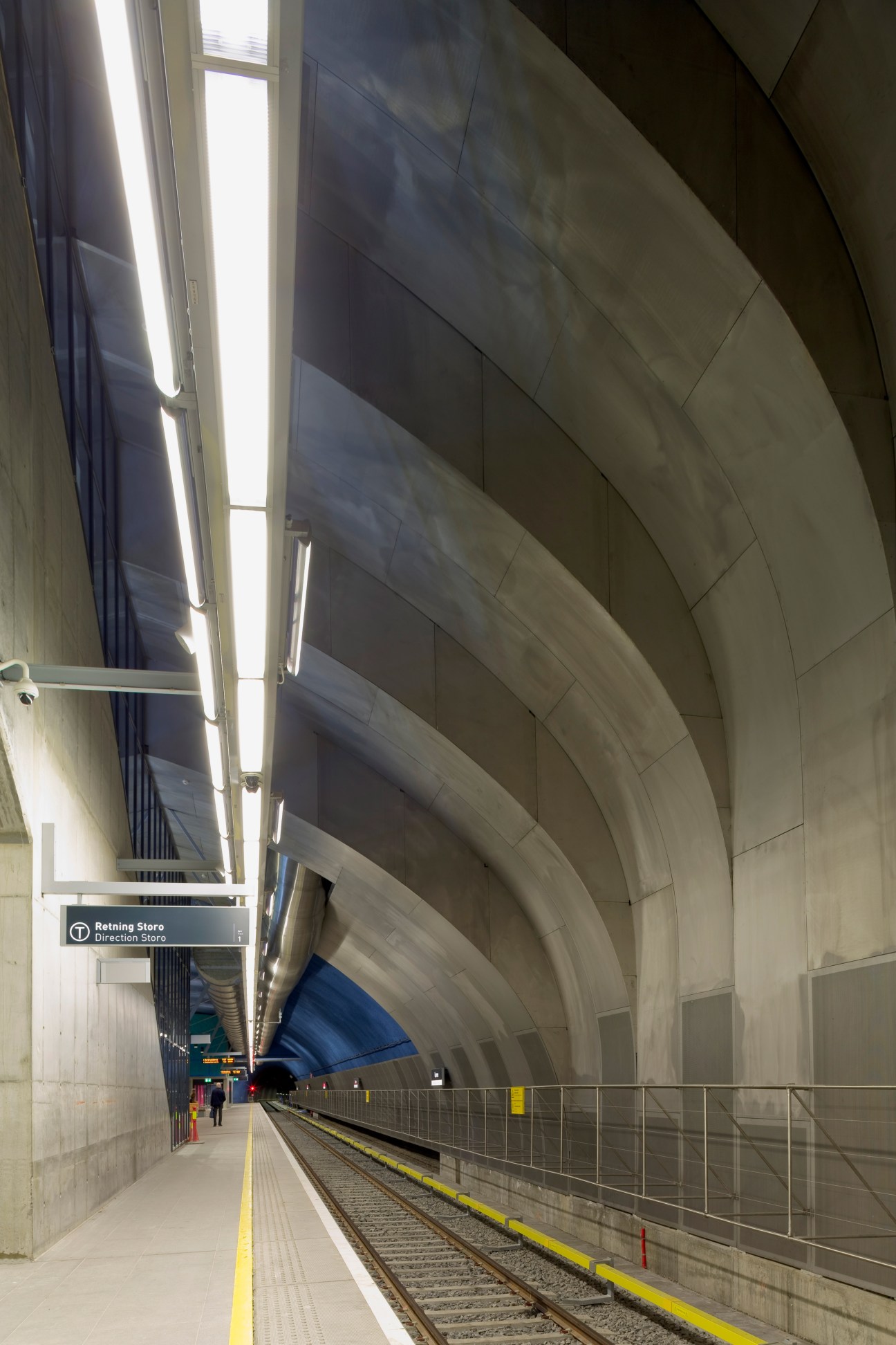 Modern train station platform with curved concrete architecture and linear ceiling lighting at Løren Station in Oslo.