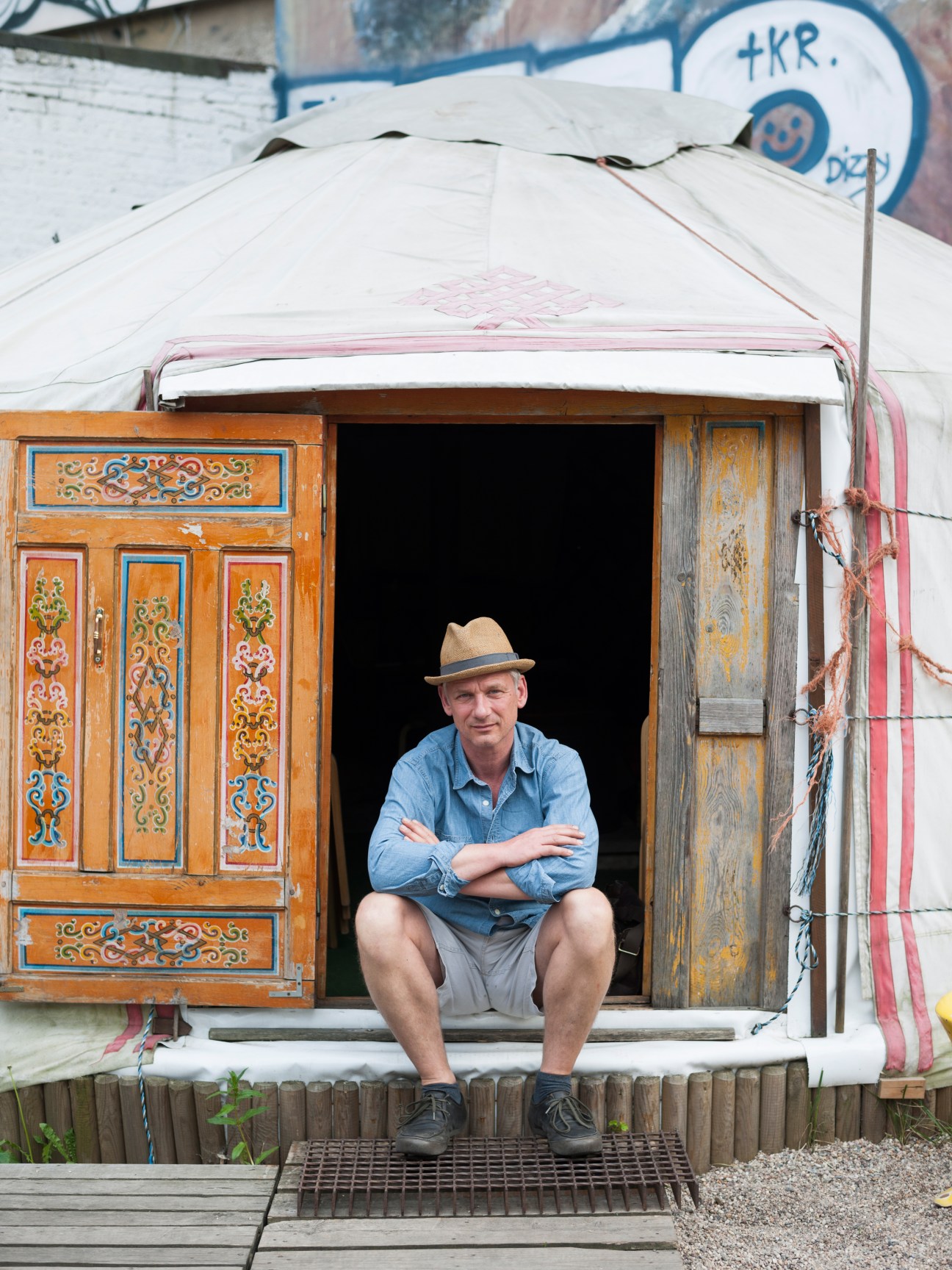 Man in hat sitting in doorway of ornately decorated wooden structure with white canvas roof